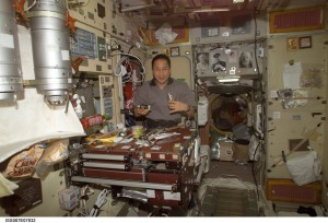 Astronaut Edward T. Lu, Expedition 7 NASA ISS science officer and flight engineer, eats a meal in the Zvezda service module on the station. The TGK system can be seen in the upper left without the ceramic mitigation screen in place. 