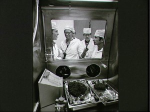 Astronauts David R. Scott, left, and James B. Irwin, right, join Manned Spacecraft Center geologists in looking at some of the first Apollo 15 samples to be opened in the Non-Sterile Nitrogen Processing Line in the Manned Spacecraft Center’s Lunar Receiving Laboratory. Holding the microphone and making recorded tapes of the two Apollo 15 crewmen’s comments is Dr. Gary Lofgren.  