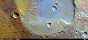 Apollinaris Patera is an ancient shield volcano measuring approximately 180 km by 280 km at its base and rising to a maximum of 5 km above the surrounding terrain. The image also shows the terrain partly covered by thin, diffuse clouds indicated by bluish-tinted areas.  