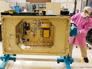 Software engineers work in the background as Glenn Research Center technician Joe Kerka rotates the SCaN Testbed flight-enclosure assembly using a specially manufactured mount.