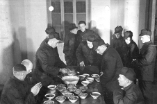 Downey and Fecteau with captured B-29 crew in a Chinese propaganda photo. (Fecteau is standing to the right of the table, reaching down for a meal. Downey stands in the center of the photo, up against the wall.)