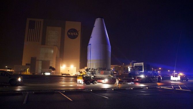 Tracking and Data Relay Satellite-K, enclosed in its payload fairing, passes through the Launch Complex 39 area and Vehicle Assembly Building at Kennedy Space Center as it travels from the Astrotech payload processing facility to its launch site.