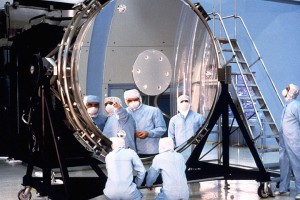Workers study Hubble’s main, eight-foot (2.4 m) mirror. The flaw in the Hubble Space Telescope’s optics was due in part to reductions in testing to save money.