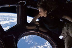NASA astronaut Tracy Caldwell Dyson, Expedition 24 flight engineer, looks through a window in the Cupola of the International Space Station. A blue and white part of Earth and the blackness of space are visible through the windows. The image was a self-portrait using natural light.