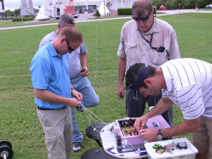 Troubleshooting avionic payload prior to a launch at Kennedy Space Center Visitor’s Center, October 2011. From left to right: Marc Butler, Curtis Brim, Larry Ludwig, and Leandro James.