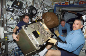 Astronauts Daniel W. Bursch (left), Expedition Four flight engineer, and Lee M. E. Morin, STS-110 mission specialist, move equipment in the Destiny laboratory on the International Space Station (ISS). Astronaut Jerry L. Ross, STS-110 mission specialist, is visible in the background. Photo Credit: NASA