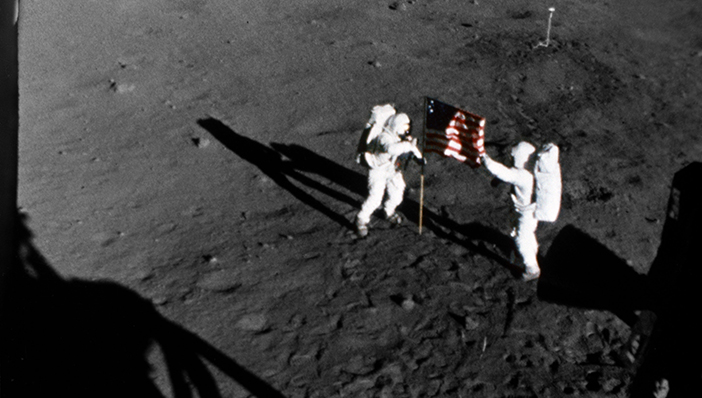 The deployment of the flag of the United States on the surface of the moon is captured on film during the first Apollo 11 lunar landing mission. Here, astronaut Neil A. Armstrong, commander, stands on the left at the flag's staff. Astronaut Edwin E. Aldrin Jr., lunar module pilot, is also pictured. The picture was taken from film exposed by the 16mm Data Acquisition Camera (DAC) which was mounted in the Lunar Module (LM). While astronauts Armstrong and Aldrin descended in the Lunar Module (LM) "Eagle" to explore the Sea of Tranquility region of the moon, astronaut Michael Collins, command module pilot, remained with the Command and Service Modules (CSM) "Columbia" in lunar orbit. Photo Credit: NASA