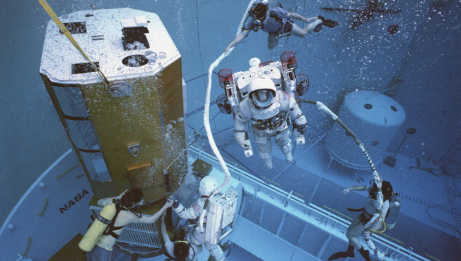NASA astronauts James D. A. “Ox” van Hoften, and George D. “Pinky” Nelson train to capture and repair the Solar Maximum Mission spacecraft at Marshall Space Flight Center’s Neutral Buoyancy Simulator. The training included using the Manned Maneuvering Unit (MMU). Credit: NASA/MSFC