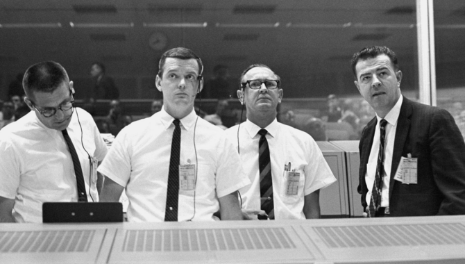 Charles W. Mathews, Manager, Project Gemini (right) stands and the flight director's console, viewing Gemini X flight display data in the Mission Control Center on July 18, 1966. With him, from left, are William C. Schneider, Mission Director; Glynn Lunney, Prime Flight Director; and Christopher C. Kraft Jr., MSC Director of Flight Operations. Credit: NASA