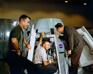 Astronauts Virgil I. Grissom (center) and John W. Young (left), prime crew for the Gemini-Titan 3 mission, are shown inspecting the inside of Gemini spacecraft at the Mission Control Center at Cape Kennedy, Florida in 1964. Riley D. McCafferty is at right. Credit: NASA