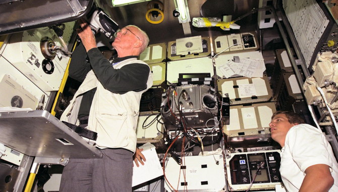 Payload Specialist John H. Glenn Jr., then a senator from Ohio, prepares to fly aboard STS-95, adjusting a video camera during training at Cape Canaveral. Mission Specialist Scott E. Parazynski looks on at right. Glenn’s two spaceflights were 36 years apart. Photo Credit: NASA