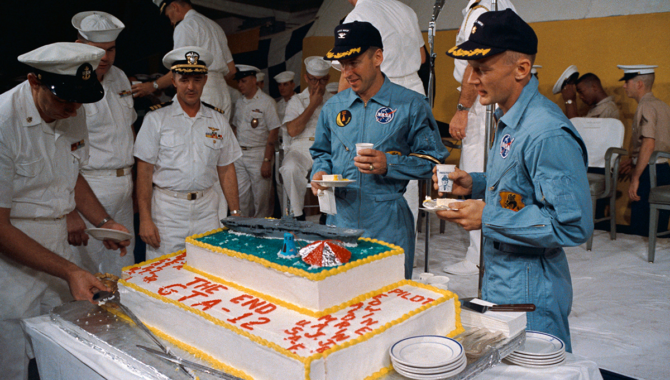 Gemini XII astronaut James A. Lovell, Jr. (left), command pilot, and Edwin E. “Buzz” Aldrin, Jr. (right), pilot, eat a piece of cake presented to the two astronauts by crew members of the prime recovery ship, USS Wasp. Gemini XII splashed down in the Atlantic Ocean at 2:21 p.m. (EST), Nov. 15, 1966, to conclude a four-day mission in space. Photo Credit: NASA