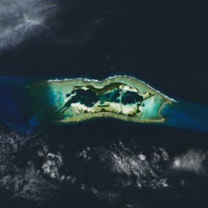 Satellite image of Palmyra Atoll, a collection of tiny islands. The atoll's coastal boundaries are turquoise compared to the rest of the ocean.