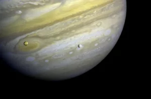 Voyager 1 took this photo of Jupiter and two of its satellites (Io, left, and Europa) on Feb. 13, 1979. Io is about 350,000 kilometers (220,000 miles) above Jupiter's Great Red Spot; Europa is about 600,000 kilometers (375,000 miles) above Jupiter's clouds. Photo Credits: NASA/JPL-Caltech