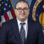 Dr. Steven Ehlert poses for his civil servant photo. Behind are the American flag and the NASA flag, partially visible on either side.