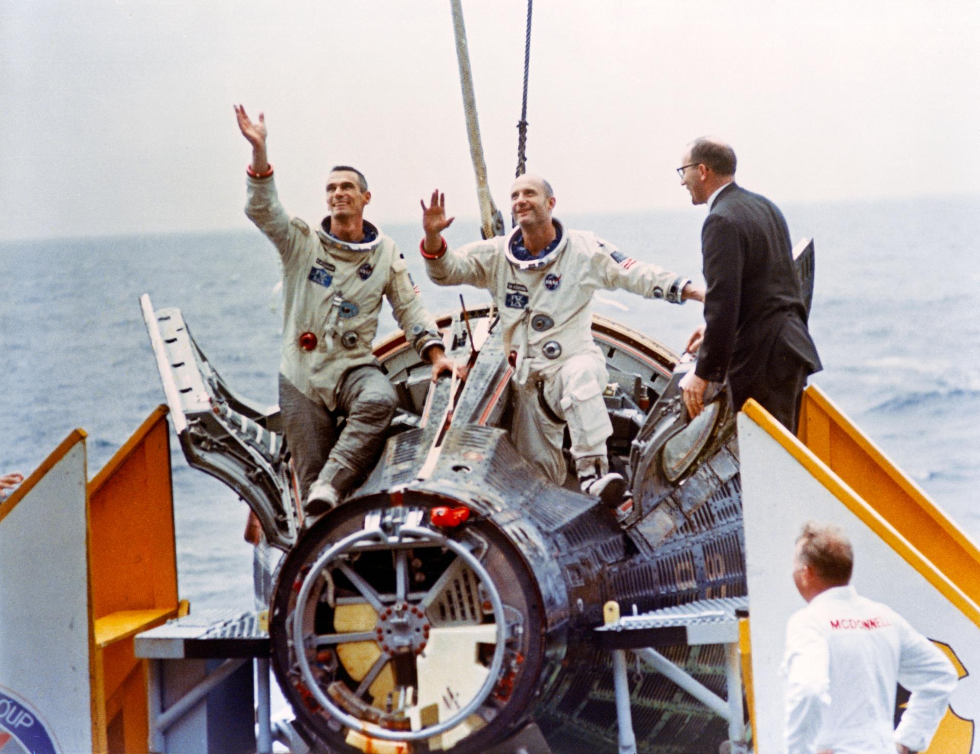 Astronauts Thomas Stafford (right) and Eugene Cernan wave to the crowd aboard the aircraft carrier USS Wasp as they emerge from their Gemini-IX-A capsule on June 6, 1966. John C. Stonesifer (far right), with the Manned Spacecraft Center’s Landing and Recovery Division, was onboard to greet the astronauts. Credit: NASA